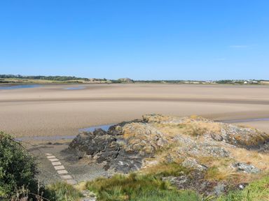 A sandy beach with rocky outcrops and green vegetation under a clear blue sky at Glanrhyd Uchaf in Llanfair yn Neubwll