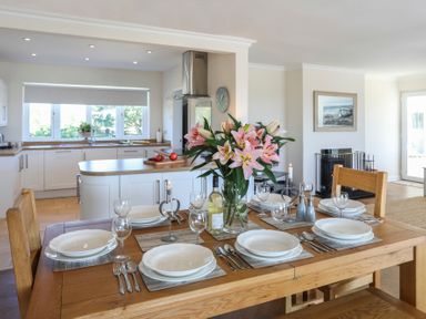 A dining table set with plates glasses cutlery and flowers in a kitchen and living area at Glanrhyd Uchaf in Llanfair yn Neubwll