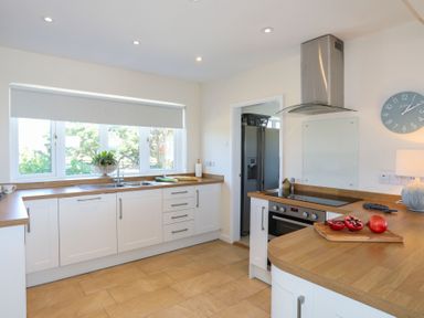 A kitchen with white cabinets wooden countertops a stove a cutting board with pomegranates and a window with a plant at Glanrhyd Uchaf in Llanfair yn Neubwll