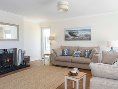 A living room with beige sofas blue cushions and a small table with cake and a cup by the fireplace at Glanrhyd Uchaf in Llanfair yn Neubwll