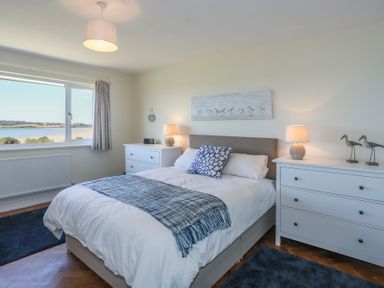 A bedroom with a bed a window two white dressers and lamps at Glanrhyd Uchaf in Llanfair yn Neubwll