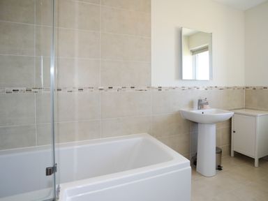 A bathroom with a bathtub a pedestal sink a wall mirror and a small white cabinet at Glanrhyd Uchaf in Llanfair yn Neubwll