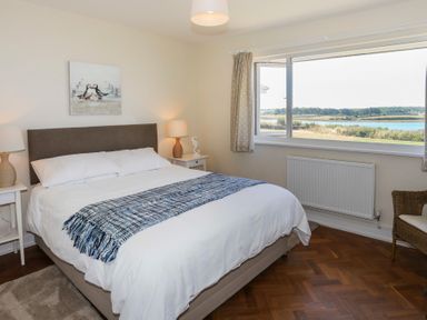 A bedroom with a bed bedside tables lamps a chair and a window with a view of water and greenery at Glanrhyd Uchaf in Llanfair yn Neubwll