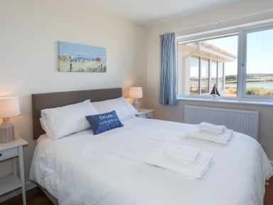 A bedroom with a bed lamps side tables and a window showing a water view at Glanrhyd Uchaf in Llanfair yn Neubwll