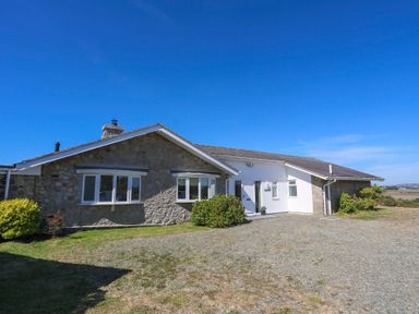 A single story house with stone and white walls with windows and a gravel driveway at Glanrhyd Uchaf in Llanfair yn Neubwll