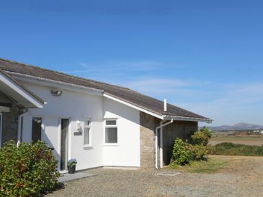 A white house with a stone wall and bushes outside under a blue sky at Glanrhyd Uchaf in Llanfair yn Neubwll