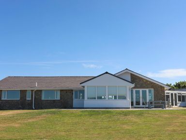 A single story house with stone and white exterior walls and multiple windows on a grassy lawn at Glanrhyd Uchaf in Llanfair yn Neubwll
