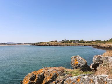 A coastal scene with rocks in the foreground water and houses on the shore at Glanrhyd Uchaf in Llanfair yn Neubwll