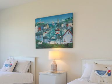 A bedroom with two single beds each with a pillow featuring a seagull illustration a white nightstand with a lamp and a nautical painting on the wall at Glanrhyd Uchaf in Llanfair yn Neubwll