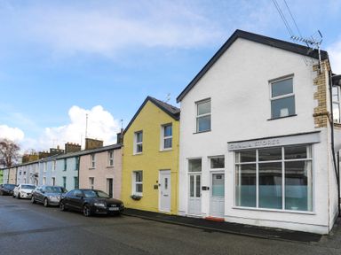 A street with parked cars and colorful row houses including Gwalia Stores in Beaumaris