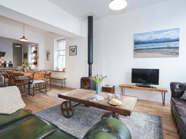 A living room with wooden coffee table, green leather sofas, TV on wooden stand, and dining table with chairs at Gwalia Stores in Beaumaris