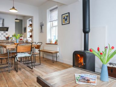 A dining area with wooden table and chairs next to a wood burning stove and a vase of tulips at Gwalia Stores in Beaumaris