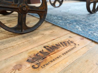 A wooden floor with a Black Daniel's Lynchburg Tennessee logo and metal wheels on a rug at Gwalia Stores in Beaumaris