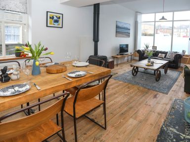A dining table set with plates and glasses next to a living area with sofas and a coffee table at Gwalia Stores in Beaumaris