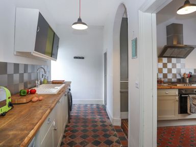 A kitchen with wooden countertops, sink, stove, and checkered floor tiles at Gwalia Stores in Beaumaris