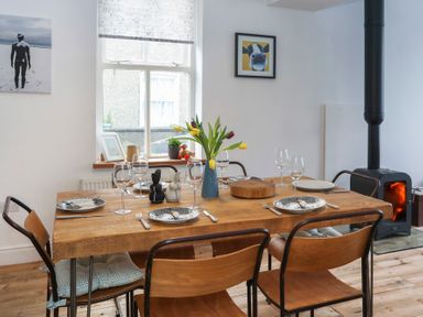 A dining room with a wooden table set for six a wood stove and framed pictures on the wall at Gwalia Stores in Beaumaris