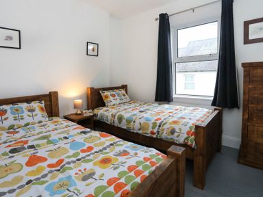 A bedroom with two single beds with colorful floral bedding a wooden nightstand with a lamp a window with dark curtains and wooden furniture at Gwalia Stores in Beaumaris