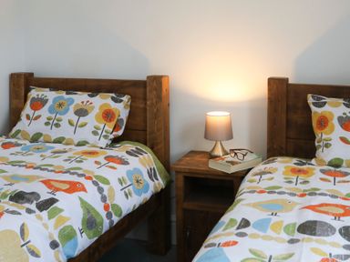 Two single beds with floral and bird patterned bedding and a wooden nightstand with a lamp a book and glasses between them at Gwalia Stores in Beaumaris