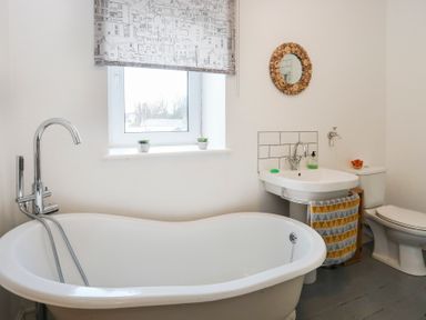 A bathroom with a freestanding bathtub sink toilet a window and a round mirror at Gwalia Stores in Beaumaris