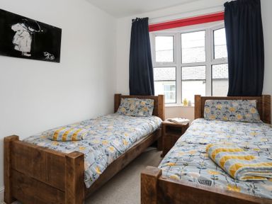 A bedroom with two wooden beds with floral bedding and a window with dark curtains at Gwalia Stores in Beaumaris