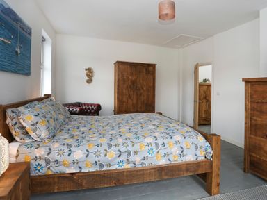 A bedroom with a wooden bed frame patterned bedspread wooden wardrobe chest of drawers and a red leather chair at Gwalia Stores Beaumaris