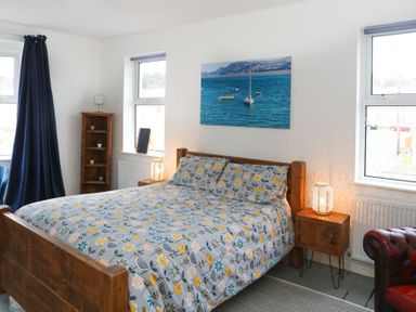 A bedroom with a wooden bed a floral bedspread a nightstand with a lamp and a wooden shelving unit at Gwalia Stores in Beaumaris