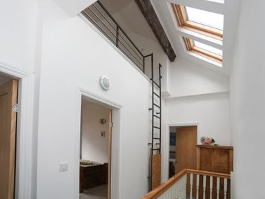 A hallway with white walls wooden doors a metal ladder two skylights and a wooden cabinet with flowers on top at Gwalia Stores Beaumaris