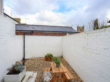 A small outdoor patio area with white brick walls gravel floor a wooden picnic table and potted plants at Gwalia Stores in Beaumaris