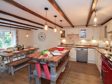 A kitchen with wooden dining table and benches and kitchen island with vegetables at Gwyndy Bach in Beddgelert