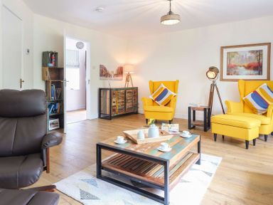 A living room with yellow armchairs a wooden coffee table and a brown chair at Gwyndy Bach in Beddgelert