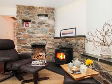 A living room with a stone fireplace a wood stove a black recliner with an ottoman and a tray with tea and cupcakes at Gwyndy Bach in Beddgelert