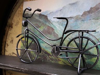 A metal wire bicycle model on a shelf with a painting of mountains in the background at Gwyndy Bach in Beddgelert