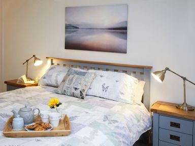 A bedroom with a bed a wooden tray with tea cups and pastries bedside tables with lamps and a wall painting at Gwyndy Bach in Beddgelert