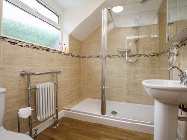 A bathroom with a shower enclosure a pedestal sink a towel radiator and a frosted window at Gwyndy Bach in Beddgelert