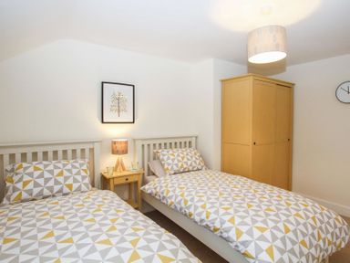 A bedroom with two single beds a yellow bedside table with a lamp a yellow wardrobe and a wall clock at Gwyndy Bach in Beddgelert
