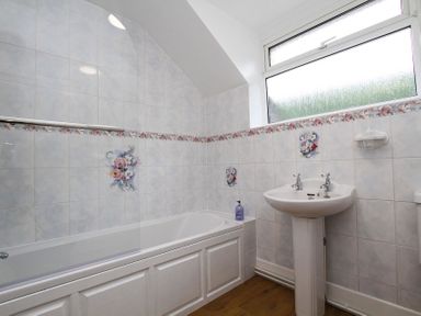 A bathroom with a bathtub sink and floral tiled walls at Gwyndy Bach in Beddgelert
