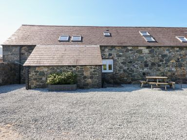 A stone building with a small bush in a planter and a wooden picnic table on a gravel ground at Hafod in Pontllyfni