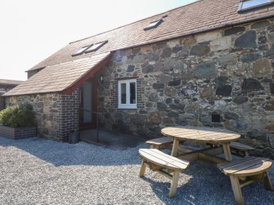 An outdoor area with a stone house wall a wooden picnic table and benches at Hafod in Pontllyfni