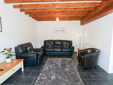 A living room with black leather sofas a grey rug wooden beams on ceiling and tiled floor at Hafod in Pontllyfni