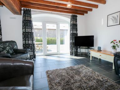 A living room with leather chairs a television on a stand and a coffee table near glass doors at Hafod in Pontllyfni