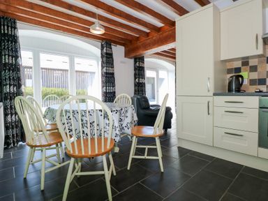 A dining area with a table and chairs next to a kitchen with cabinets and appliances at Hafod in Pontllyfni