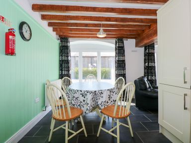 A dining area with a round table and six chairs under wooden beams at Hafod in Pontllyfni