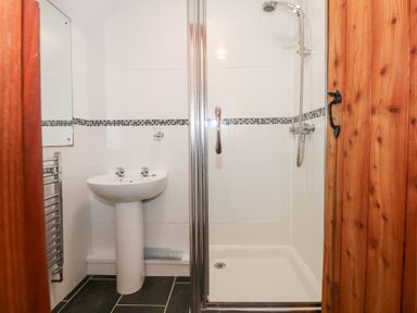 A bathroom with a white pedestal sink a shower with glass doors and a wooden door at Hafod in Pontllyfni