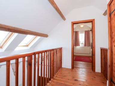 A wooden gallery hallway with exposed beams skylights and a doorway leading to a room with a window and curtains at Hafod in Pontllyfni