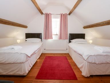 A bedroom with two single beds a red rug wooden floor and pink curtains at Hafod in Pontllyfni