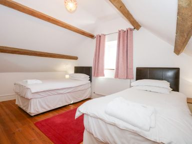 A bedroom with two single beds wooden ceiling beams a red rug and pink curtains at Hafod Pontllyfni