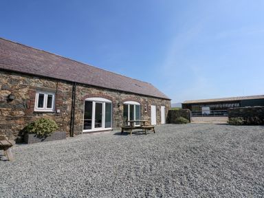 A stone building with white doors and windows a wooden picnic table and gravel ground at Hafod in Pontllyfni