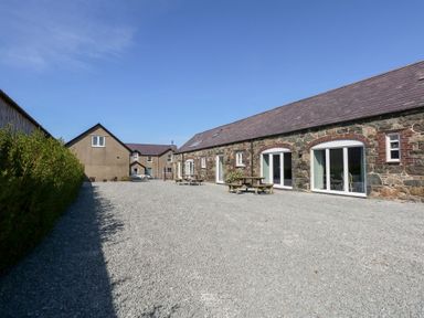 An outdoor gravel area with picnic tables beside a stone building with multiple windows at Hafod in Pontllyfni