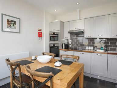 A kitchen with a wooden dining table and four chairs next to cabinets and appliances at Harlech Apartments - Branwen in Harlech