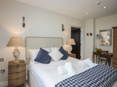 A bedroom with a bed with pillows and rolled towels bedside tables with lamps and a desk with a chair at Harlech Apartments - Branwen in Harlech